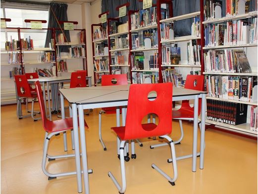 Table blanche avec des chaises rouges, étagères remplis de livres le long du mur.