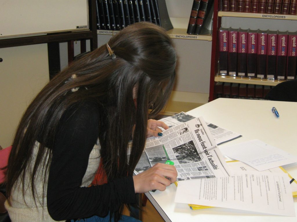 Élève assise à une table travaillant avec des photocopies de journaux.