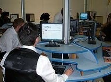 Photo salle informatique, bureaux circulaires bleus en bois, élève vu de dos face à un écran.
